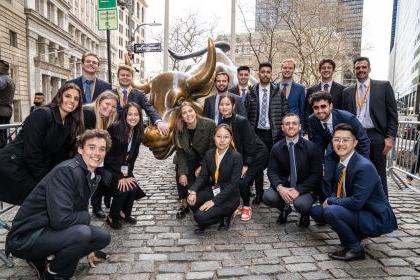 students stand next to the bull of Wall Street statue