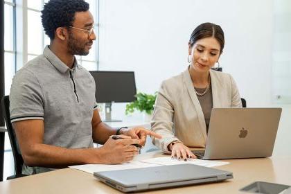 Two people sit at a desk looking at a computer together